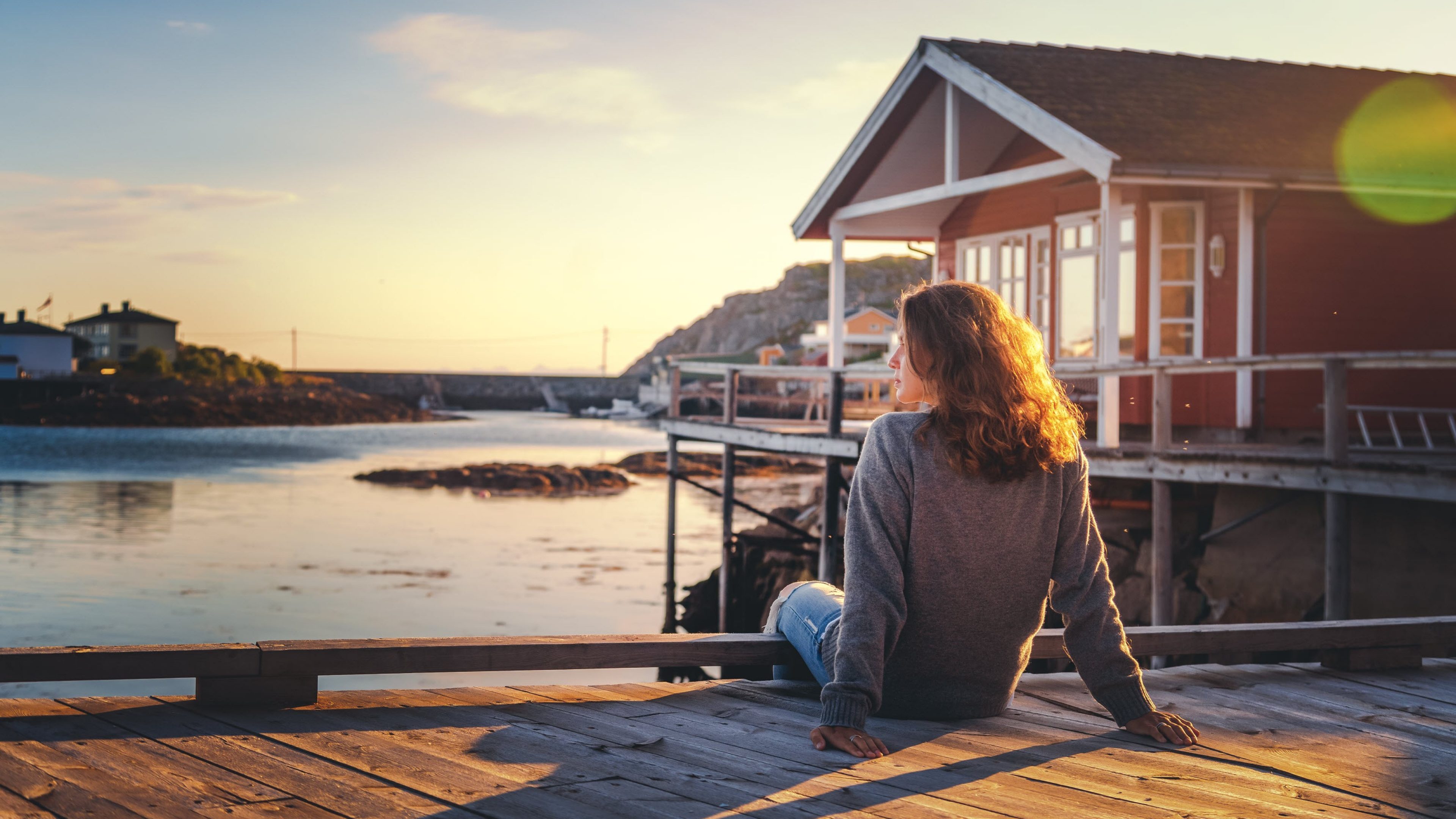 Beautiful young  girl traveler sitting on wooden pier on the background of traditional red rorbu traveling to Lofoten Norway